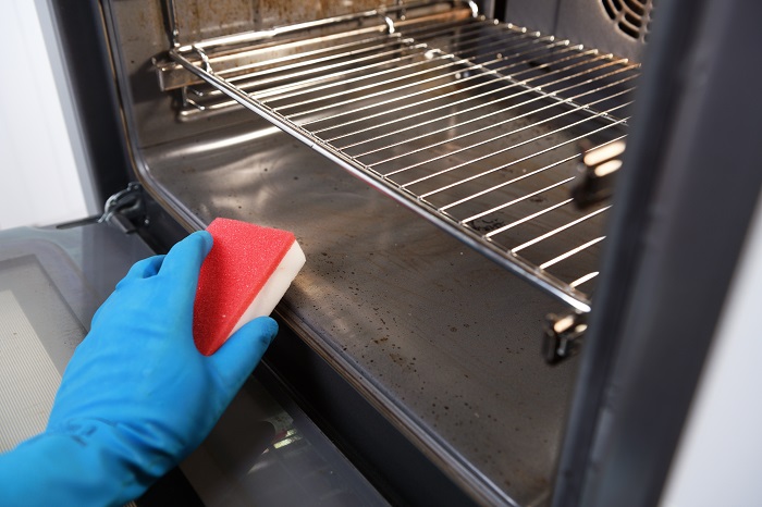 Rubber gloved hand cleaning the inside of an oven with a sponge.