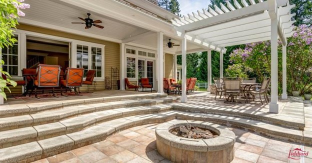 Modern backyard with stone pavement, a fire pit, multiple dining tables, and an overhead onning.