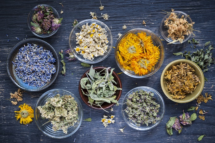 Various bowls of flowers and herbs sitting on a wooden table.