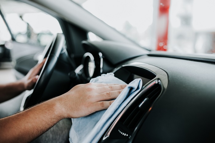 A man wiping down the interior of a car with a wash rag. 