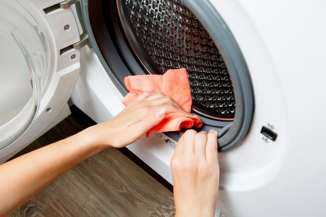 closeup view of an arm using an orange cloth to wipe down the seal of a front load washer
