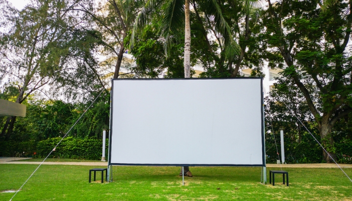 A large projector screen stand is setup outside on the lawn