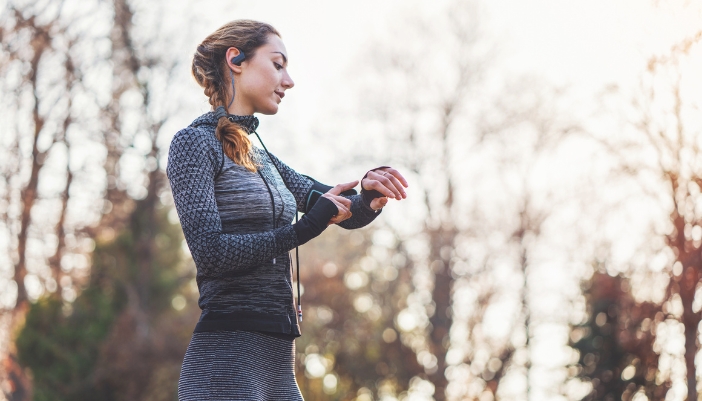 Woman wearing waterproof earphones and a fitness tracker while taking a springtime run