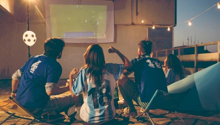 Group of people cheering soccer match on projector screen