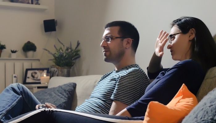woman covering her eyes while watching TV with man