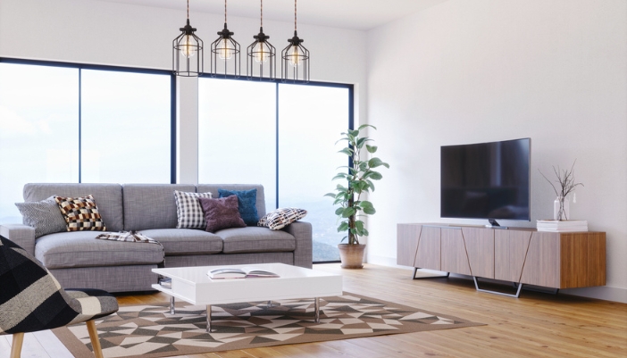 Brightly lit modern living room with a gray L-shaped couch and a large flat TV.