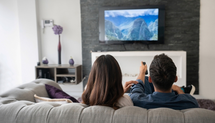 A couple sits on a couch and watches a movie together.