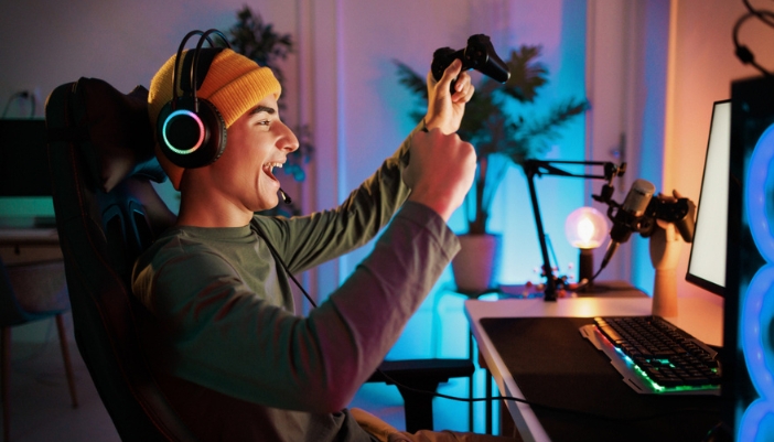 A young boy sits at his gaming computer and celebrates a win.