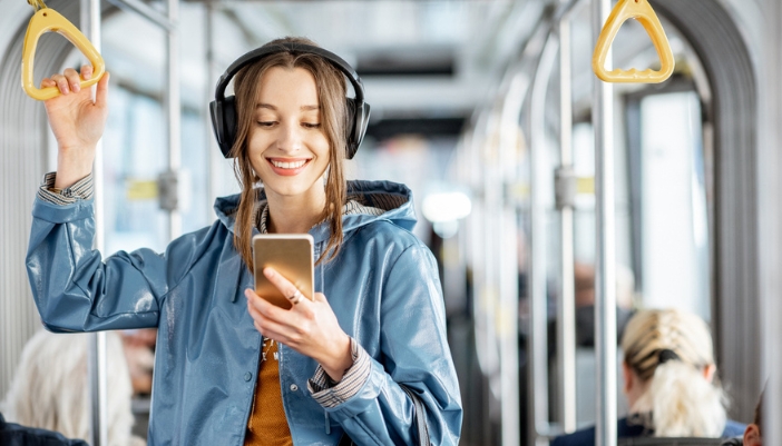 A woman riding a bus checks her phone while wearing headphones.