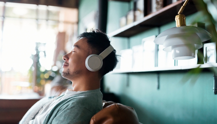 A man sits and relaxes on his couch with headphones on.