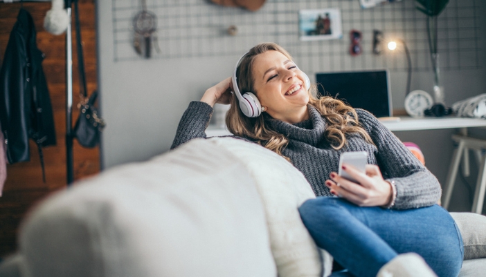 A woman sits on her couch at home and happily listens to her headphones.