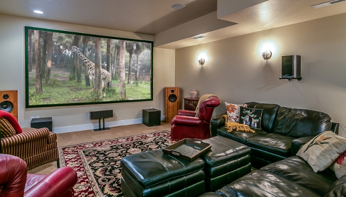 A home theater with black leather furniture, surround sound, and a projector TV.