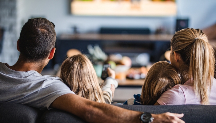 A family settles in on a couch together to watch a movie together.