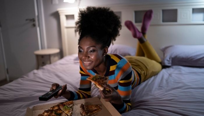 woman eating pizza and watch tv in bed