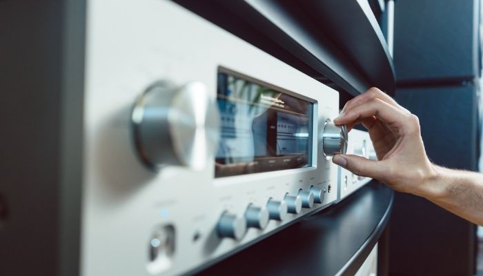 Hand turning up volume of Hi-Fi amplifier in her home