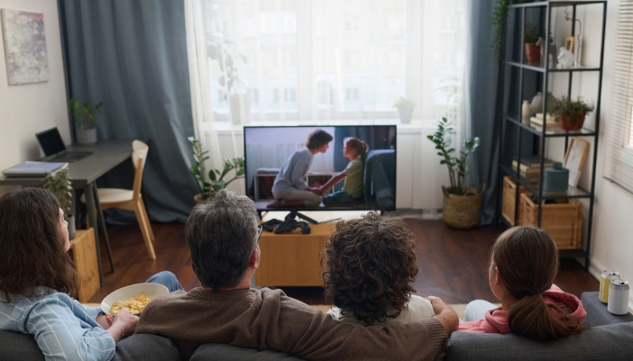 Family watching TV in front of big window with the curtains open