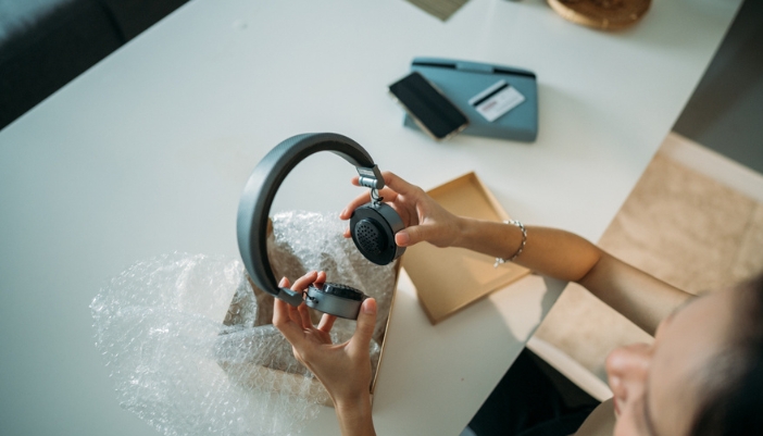 A pair of female hands unbox a pair of headphones at home.