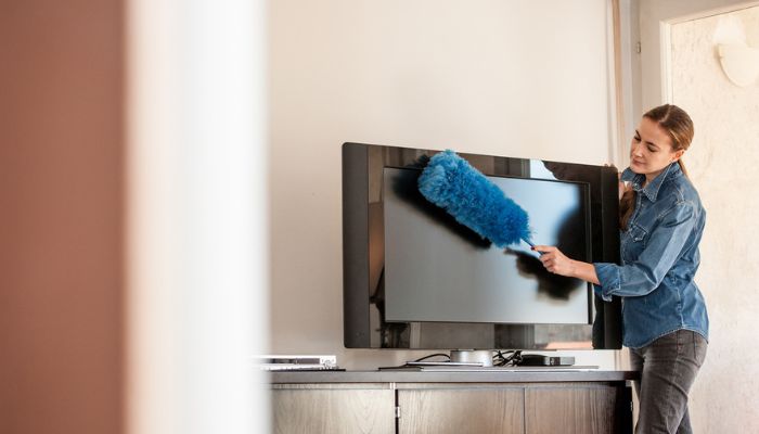 Woman dusting tv with blue duster