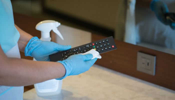 hands with gloves cleaning the tv remote control