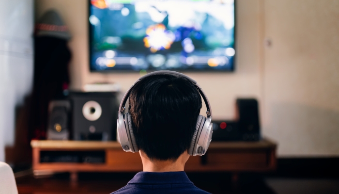 Kid playing video games with high-quality headphones, with a speaker system in the background as an alternative