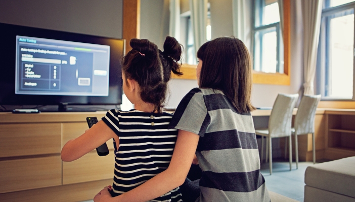Two young girls adjusting the settings on their TV