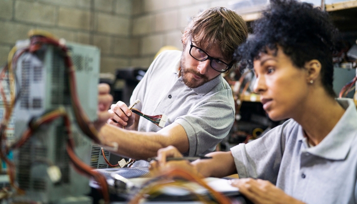 Two people breaking down electronics for recycling