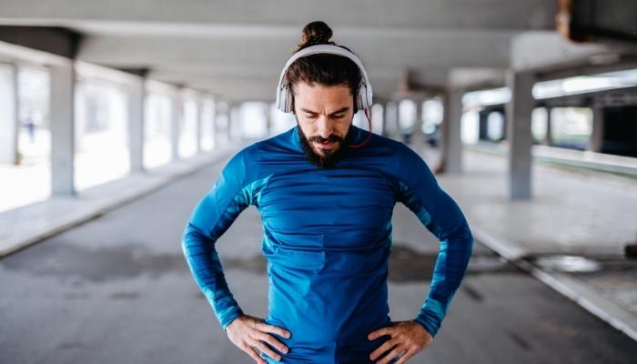 Man in a blue shirt and white wireless headphones getting ready to exercise