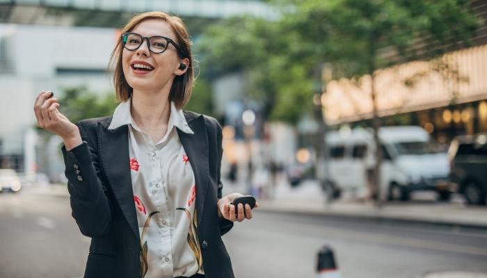 Woman walking on the street and talking on the phone with wireless headphones 