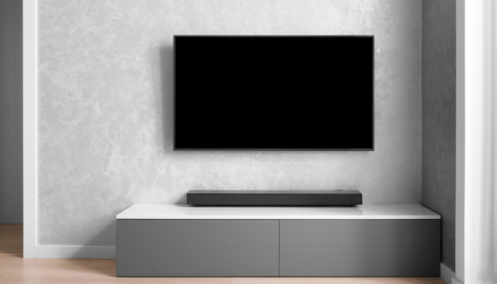 A blank flat screen tv on a gray wall with a sound bar beneath it.
