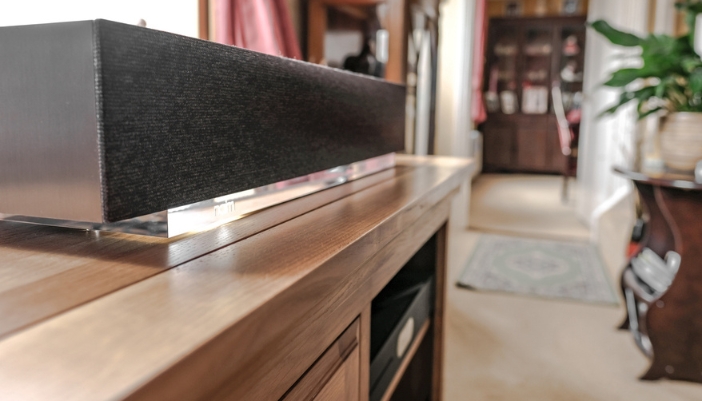 A close-up of a black sound bar on a wooden console center.