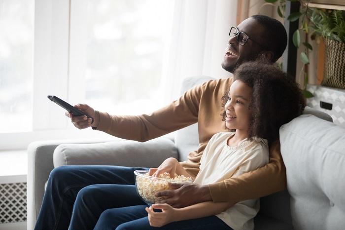 Dad relaxing on the couch with his daughter watching TV together. 