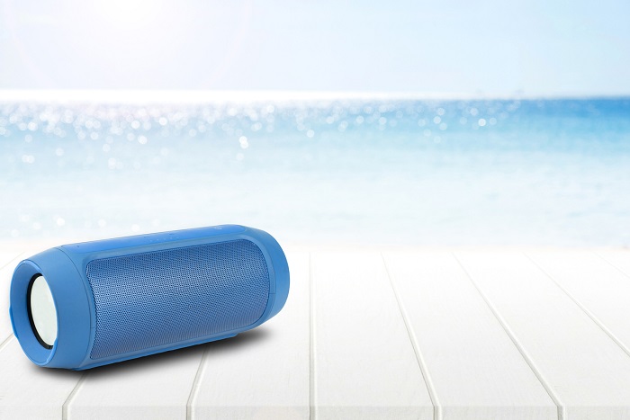 A portable speaker sitting in direct sunlight with a beach backdrop