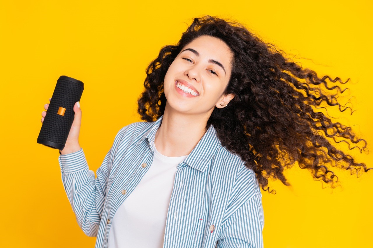 Woman in a hat and jacket joyously listens and grooves to music on her portable speaker outdoors 