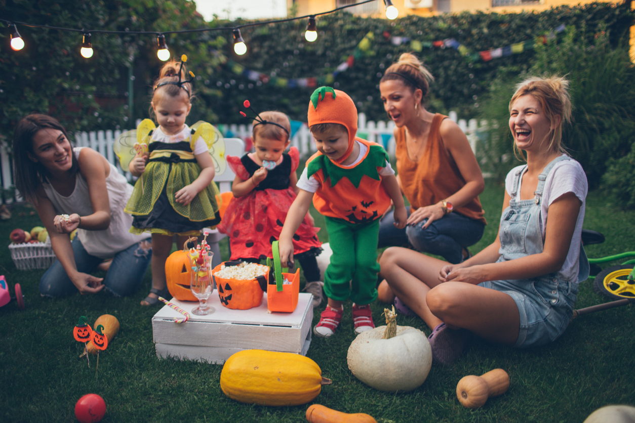 mothers with children in Halloween costumers watch movie outside with popcorn