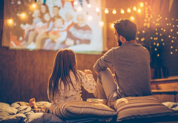 Father and daughter watching a movie with a projector set up in the backyard