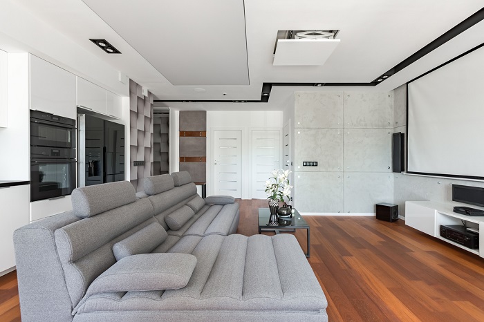 Modern living room with in-ceiling projector, projector screen, sofa and kitchenette