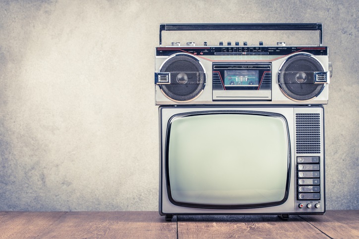 Retro old TV set receiver and radio cassette recorder on table front textured concrete wall background.