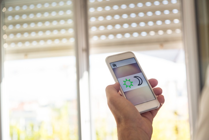 Hand holding smart phone controls blinds with an app