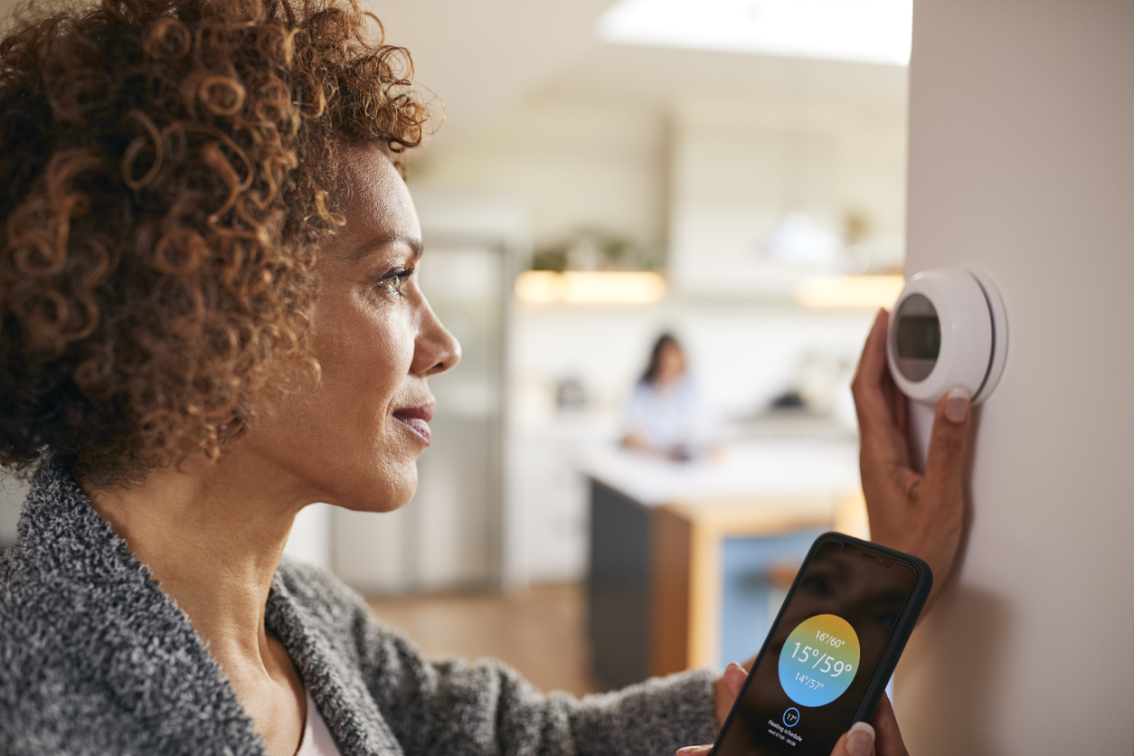 woman uses app on smartphone to control smart thermostat at home
