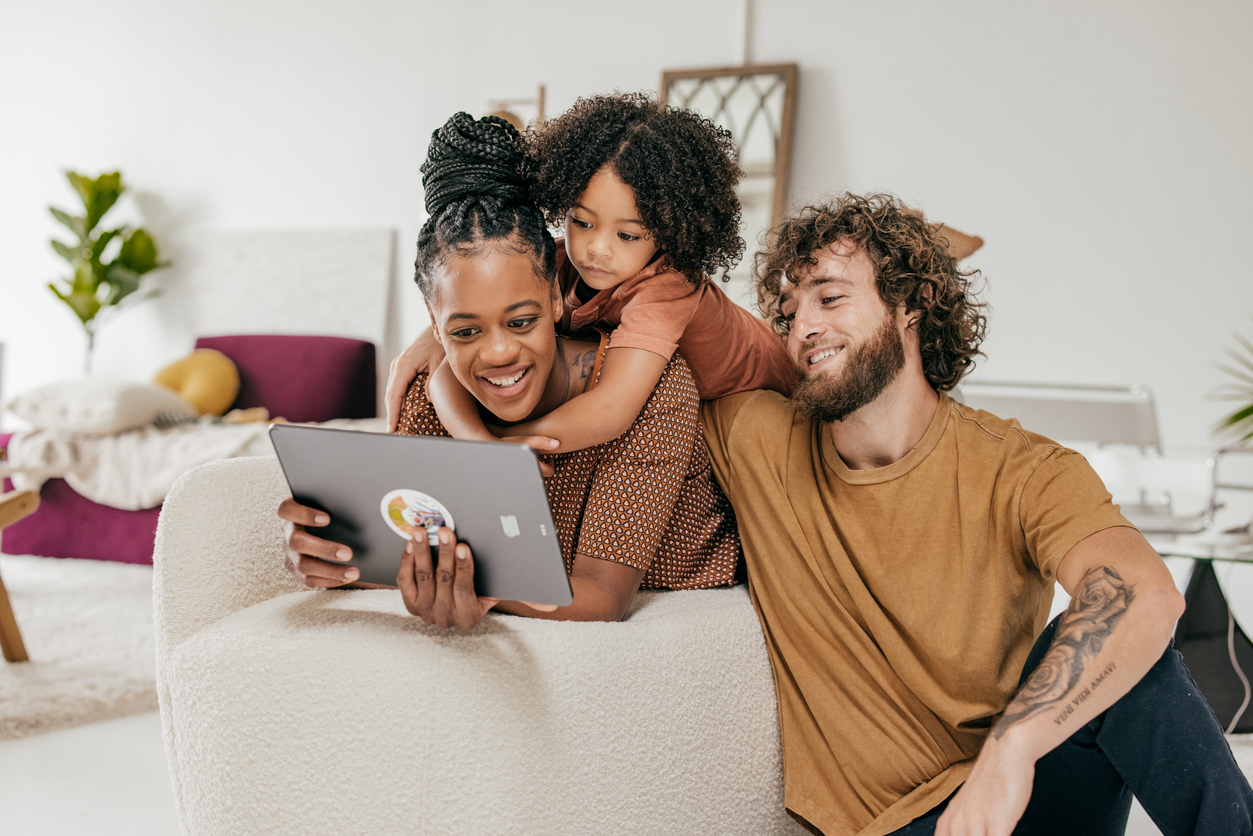 family of three sitting on their living room sofa with tablet