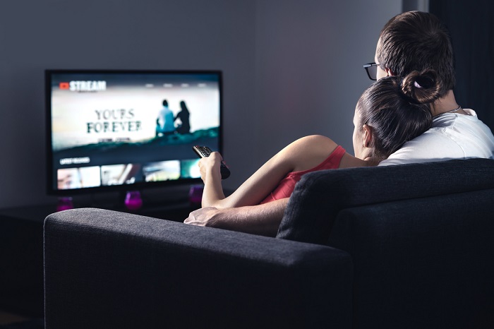 Couple watching TV on the couch cuddled together.