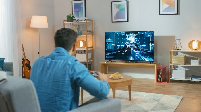 Man sits on the couch playing video game on TV.