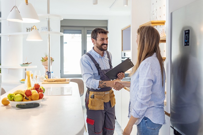 Service worker shaking hands with a woman in a modern kitchen.