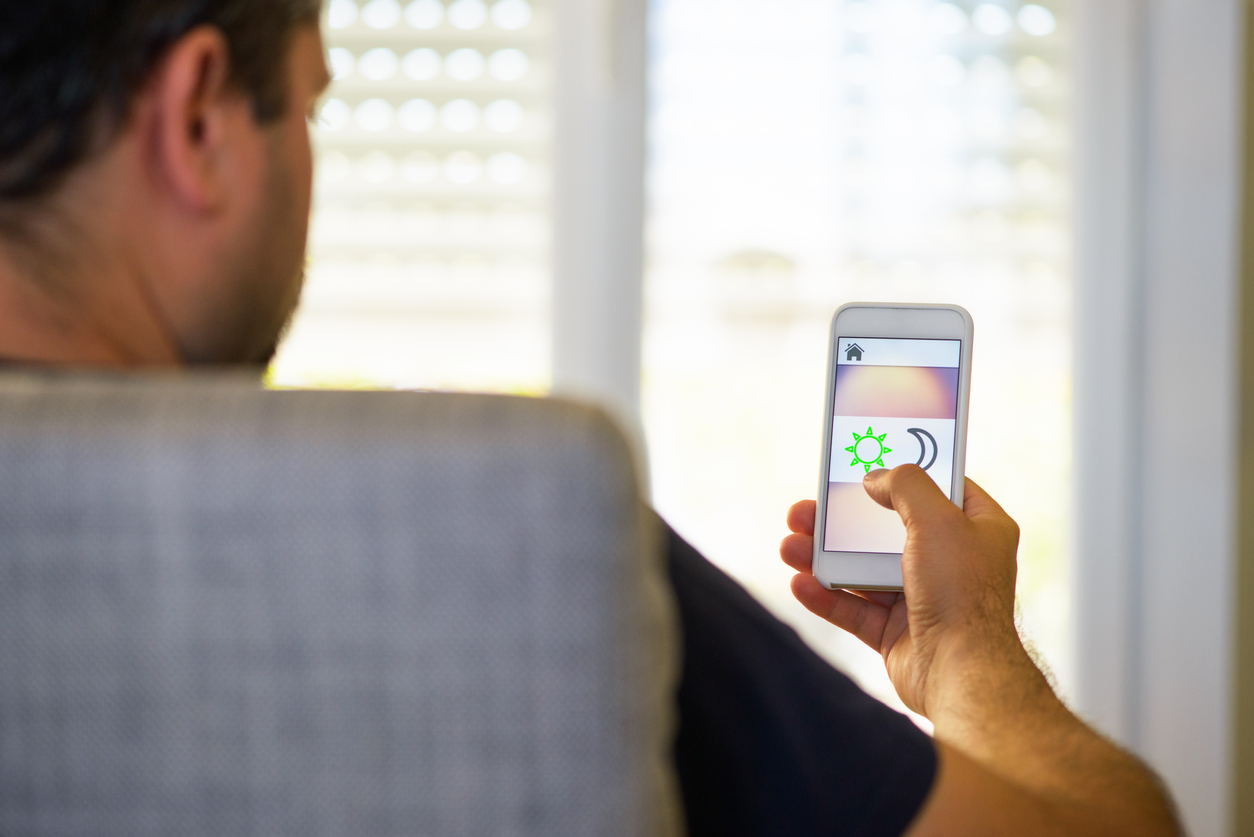 Man sitting at home, using a smart shades or blinds application on a smart phone.