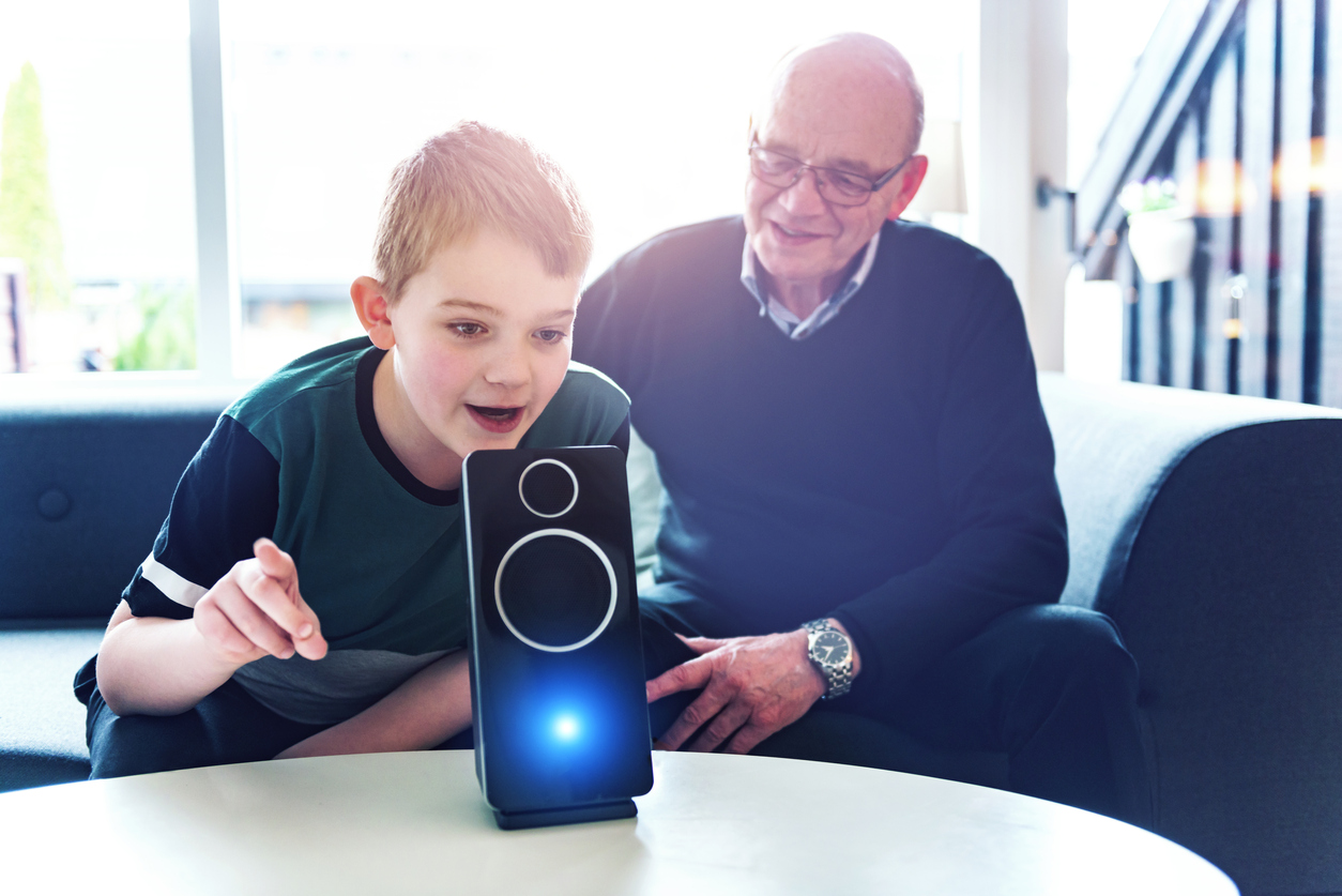 A boy and his grandfather voice control a digital assistant in their living room