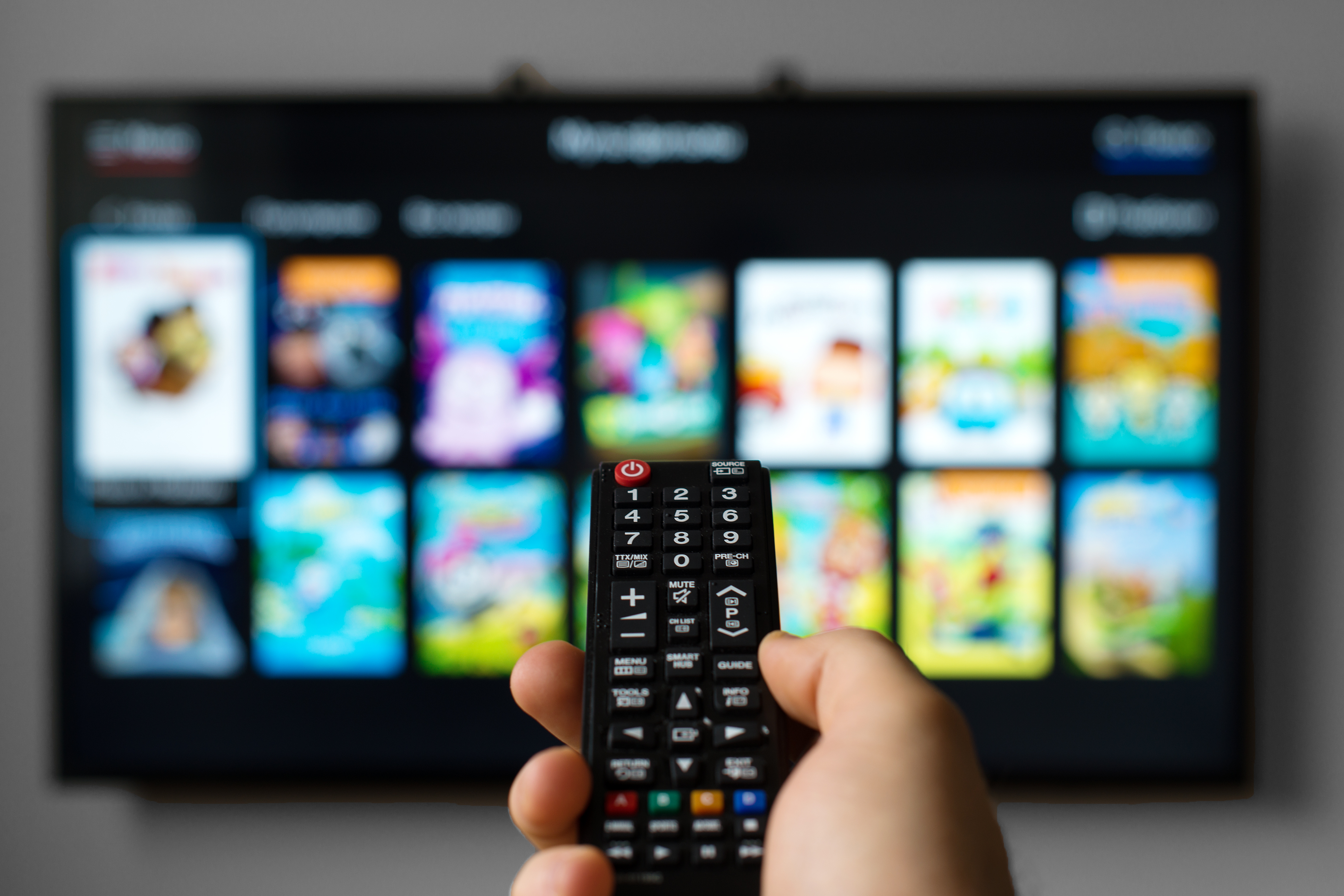 First-person shot of a hand holding a TV remote to make a selection from a TV screen