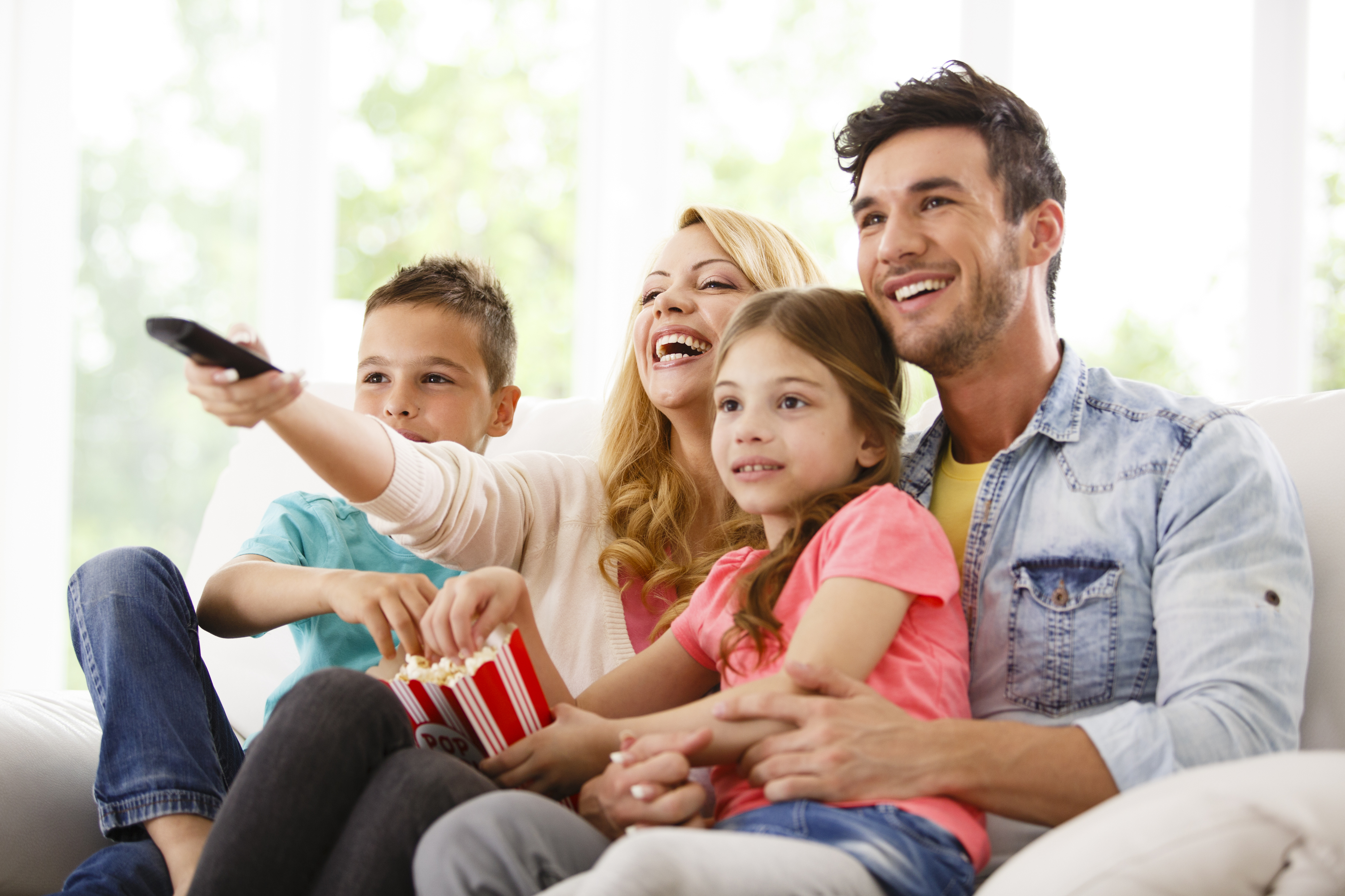 Father, mother, son, and daughter enjoy TV with popcorn on the couch