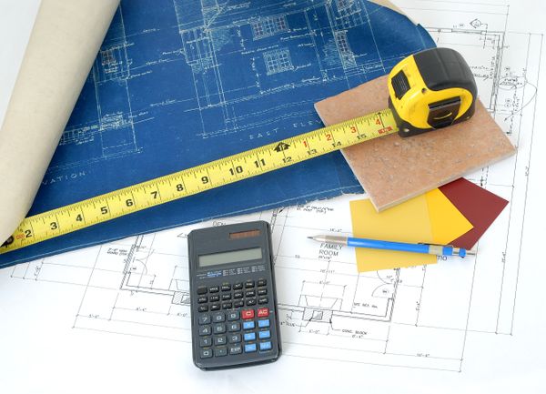 Overhead shot of a blueprint, tape measurer, calculator, and tile sample