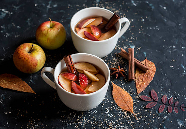 two cups of apple cider with apples, cinnamon, and cloves on the table