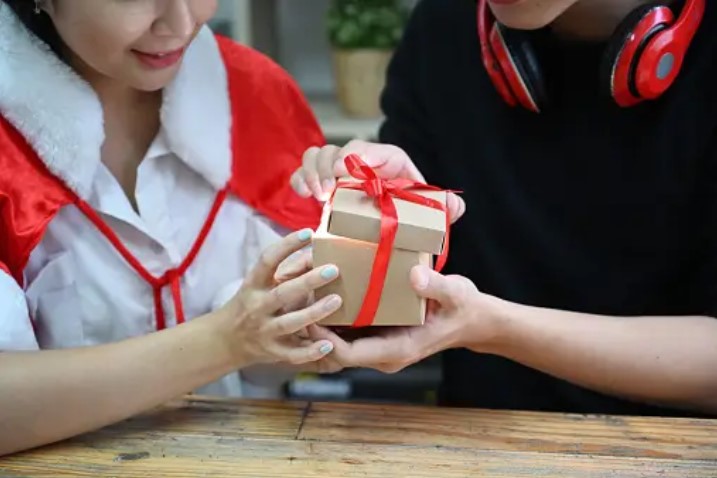 close up shot of a box with two people sitting at a table with one opening the gift box